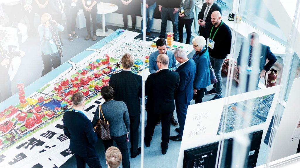 Mehrere Personen um einen großen Tisch mit Modell einer digitalen Stadt