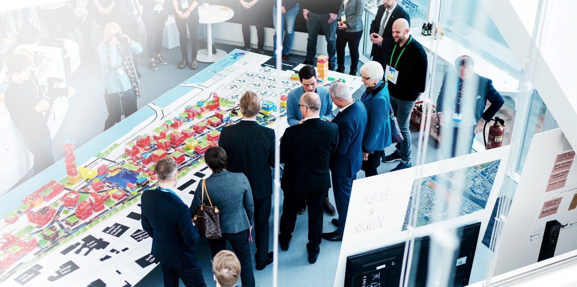 Mehrere Personen um einen großen Tisch mit Modell einer digitalen Stadt